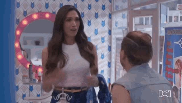 a woman in a white tank top is talking to another woman in a store