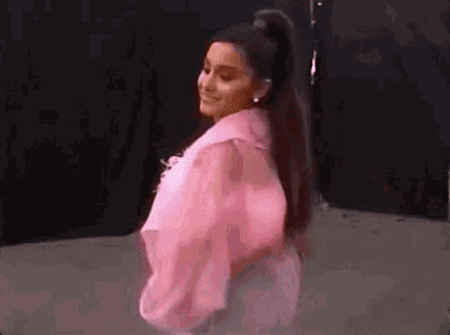 ariana grande is wearing a pink jacket and a ponytail while dancing on stage .