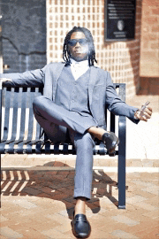 a man in a suit sits on a bench with his legs crossed and smoking a cigar