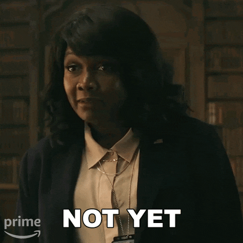 a woman in a suit says " not yet " in front of a bookshelf