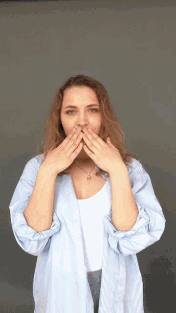 a woman covering her mouth with her hands while wearing a striped shirt