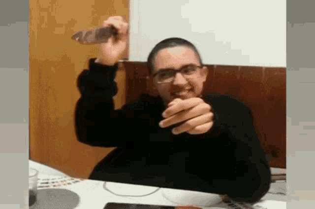 a man with glasses is sitting at a table holding a bottle of beer in his hand .