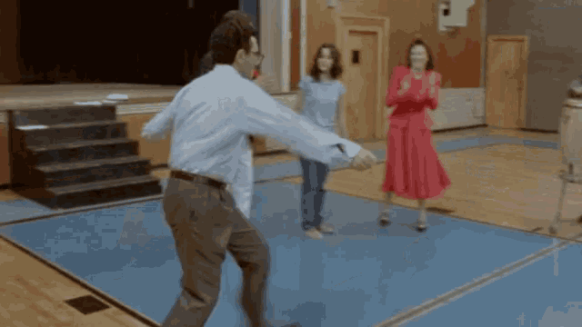 a man in a blue shirt is dancing in a gym with two women