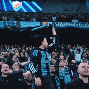 a boy in a blue adidas shirt stands in front of a crowd of people