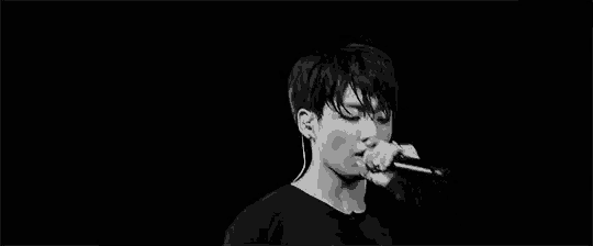 a black and white photo of a young man singing into a microphone on a stage .