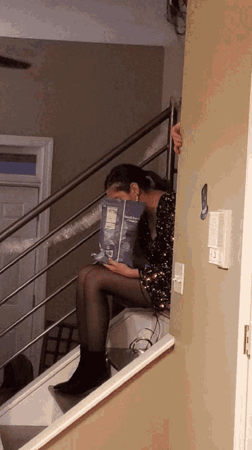 a woman sits on a set of stairs holding a box of kraft macaroni & cheese