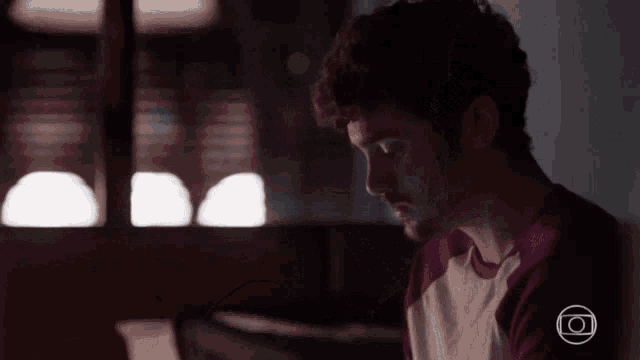 a man is sitting in a dark room looking at a laptop .