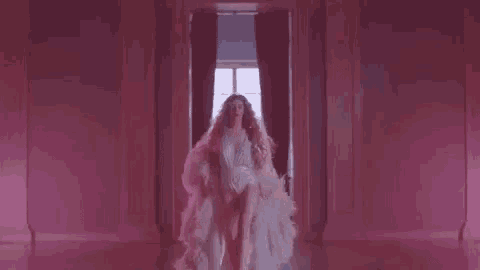 a woman is standing in a pink room wearing a white robe and a white bodysuit .