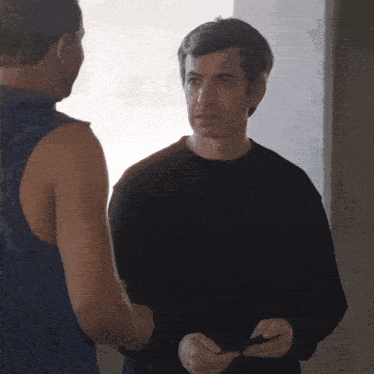 a man in a black sweater is talking to another man in a blue tank top
