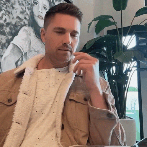 a man in a tan jacket is sitting in front of a picture of a girl