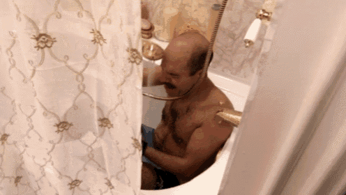 a bald man with a mustache is sitting in a bathtub with a shower curtain