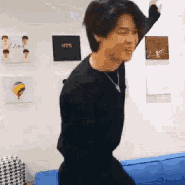 a man in a black shirt is dancing on a blue couch in a room .