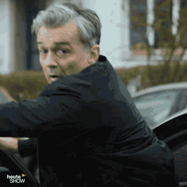 a man in a suit is getting out of a car with the words heute show behind him