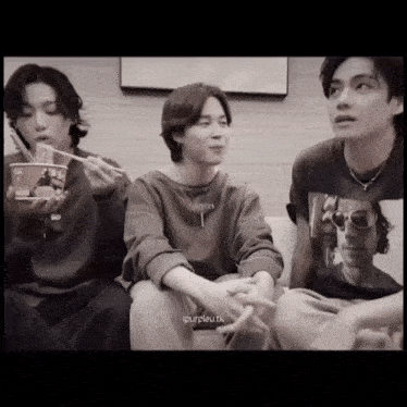 a group of young men are sitting on a couch and one of them is eating noodles