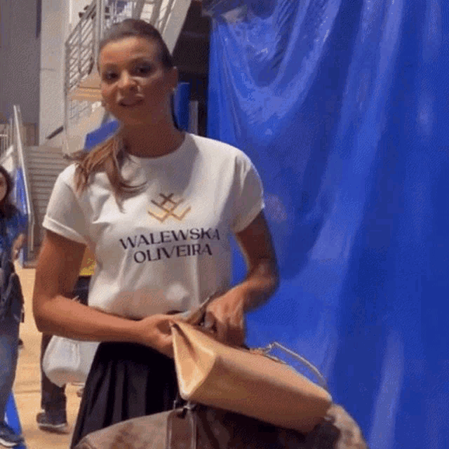 a woman wearing a t-shirt that says walewska oliveira is holding a purse .