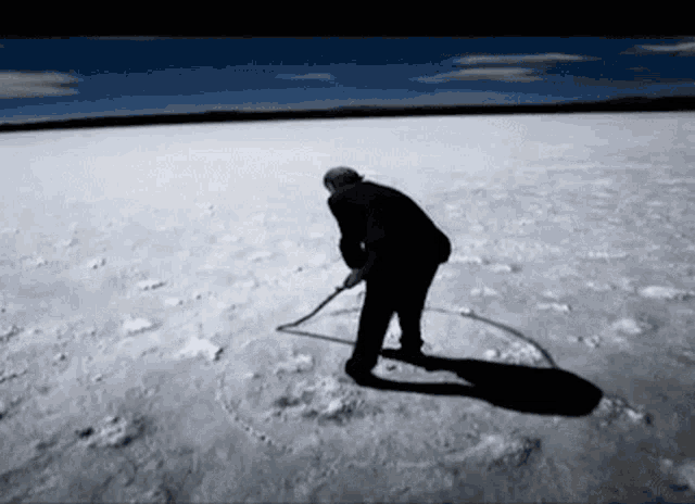 a man is standing in a snowy field holding a stick