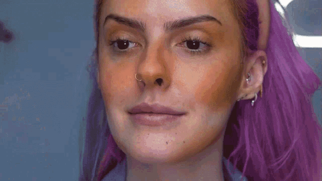 a woman with purple hair and a nose ring smiles