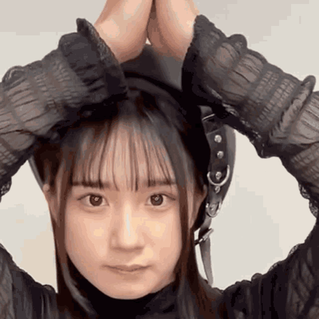 a close up of a woman 's face with her hands on her head making a heart shape