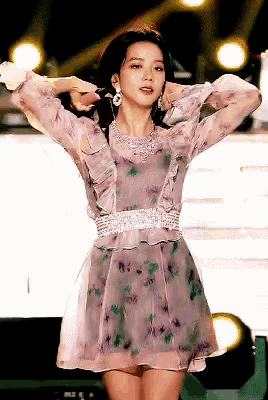 a woman in a floral dress is standing on a stage with her hands behind her head