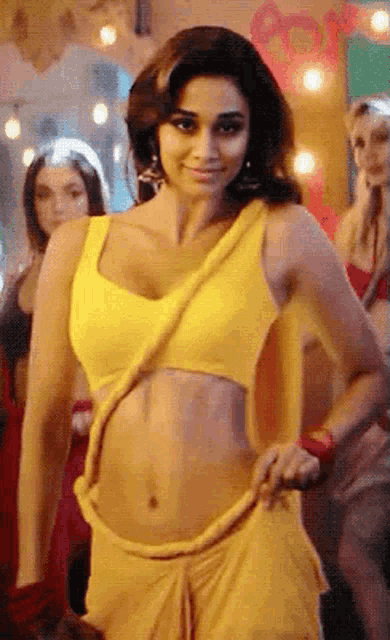a woman in a yellow crop top and a yellow skirt is dancing in a room .