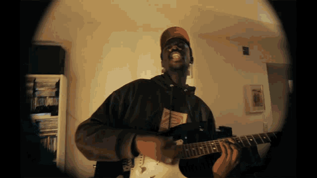 a man playing a guitar in a room with a picture on the wall that says ' a ' on it