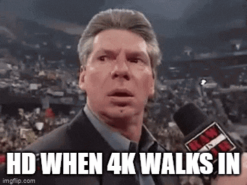 a man in a suit is talking into a microphone in front of a crowd in a stadium .