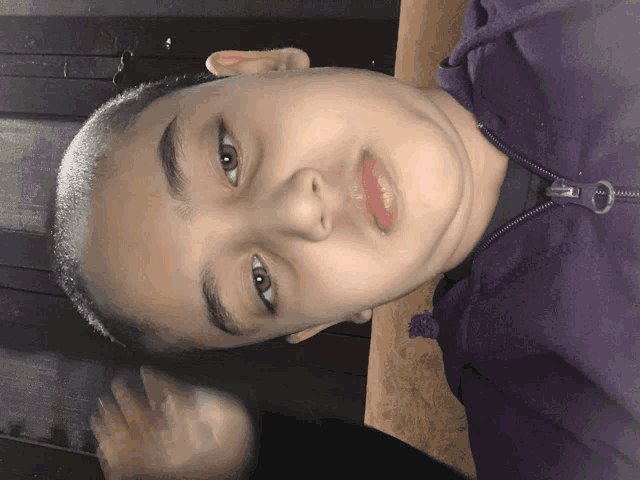 a young boy wearing a purple jacket looks down at something