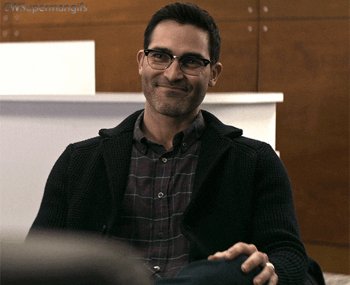 a man wearing glasses and a plaid shirt smiles while sitting down
