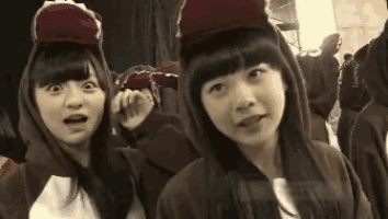 two girls wearing hoodies and hats are standing next to each other and looking at the camera .