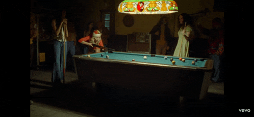 a group of people playing pool under a stained glass light