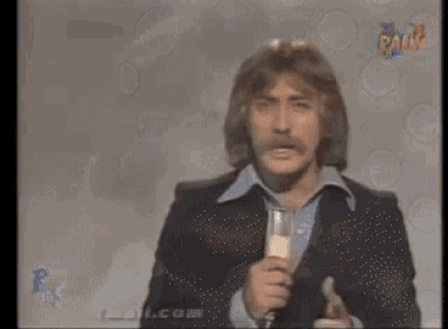 a man in a suit is holding a microphone in front of a screen that says rams