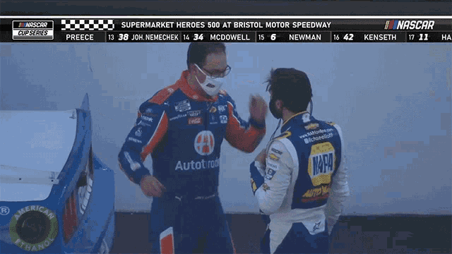 a man wearing a napa shirt talks to another man wearing a face mask