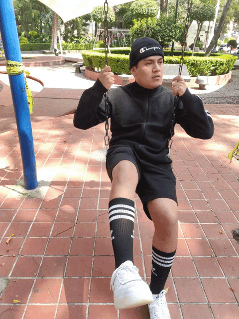a boy wearing a champion hat sits on a swing in a park
