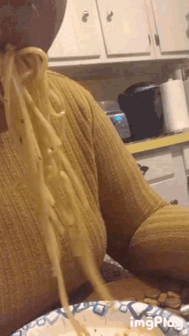 a woman in a yellow sweater is eating spaghetti