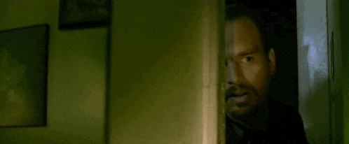 a man with a beard is standing in a dark room looking out of a doorway .