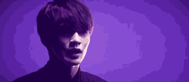 a man in a black shirt is standing in front of a purple background .