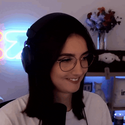 a woman wearing headphones and glasses smiles in front of a neon sign that says ' e2 '