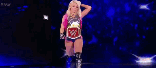 a female wrestler is walking on a stage with a wrestling belt .