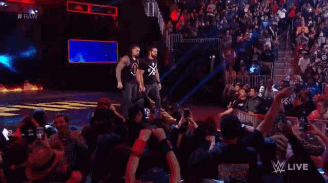 roman reigns and seth rollins are walking on a wrestling ring .