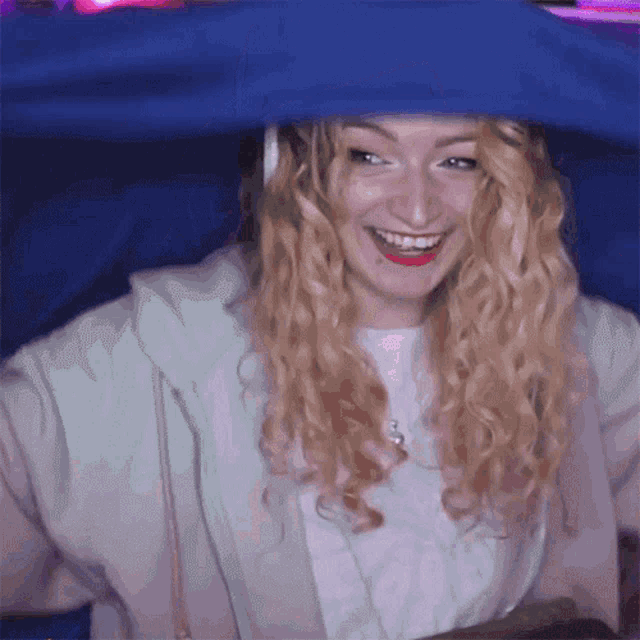 a woman with curly blonde hair is smiling under a blue tarp
