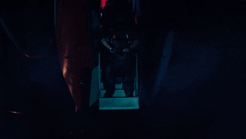 a group of people are standing in a dark room with a red light behind them that says ' emergency exit '