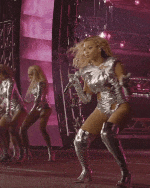 a woman in a silver bodysuit and silver boots is dancing on stage