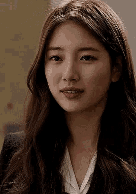 a close up of a woman 's face with long hair wearing a suit and a white shirt .