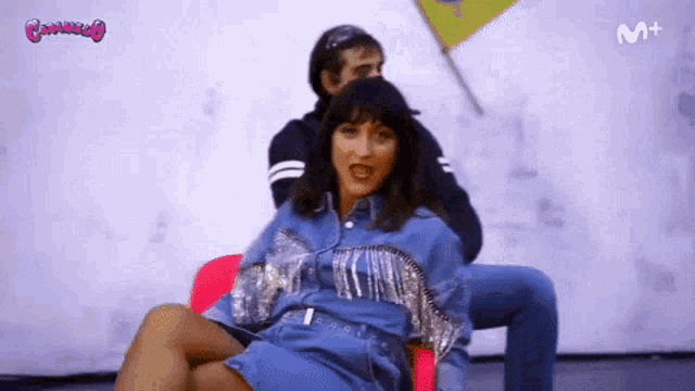 a woman in a blue dress is sitting next to a man in a denim jacket with the letters m + on the bottom