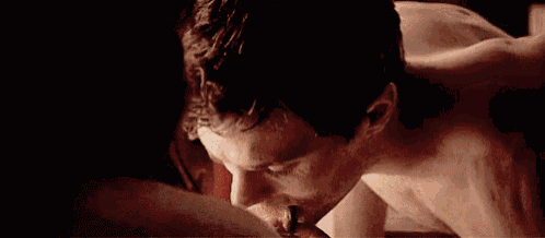 a shirtless man is eating a piece of pizza while laying on a bed with a woman .