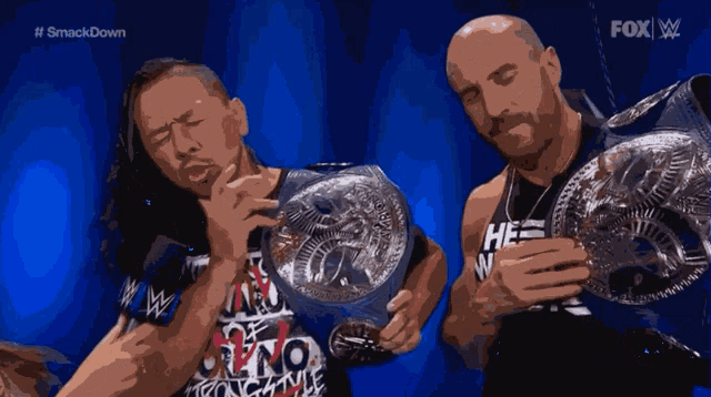 two wrestlers are holding their championship belts in front of a blue background that says #smackdown