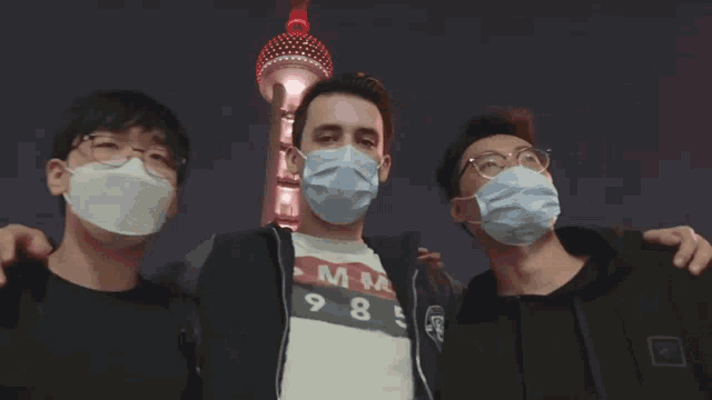 three men wearing face masks are posing for a picture with a tower in the background