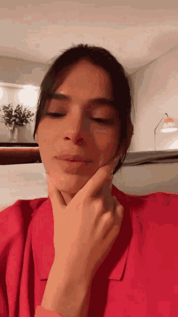 a woman in a red shirt holds her hand to her face