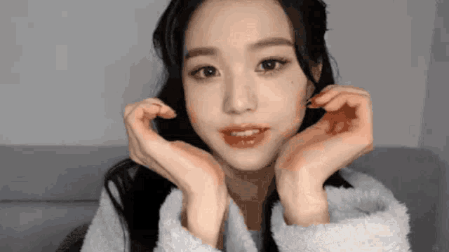 a woman is making a heart shape with her hands on her face .