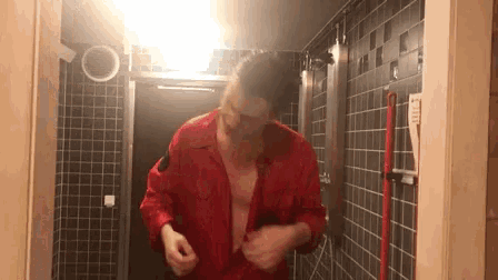 a man in a red shirt is standing in front of a mirror in a bathroom .